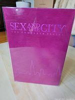 Pink velvet boxed set with the title 'Sex and the City The Complete Series' embossed on the cover with city skyline illustration.