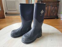 Pair of black Muck Boot Company steel toed boots on hardwood floor.