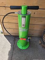 Front view of green Steam Whistle bike tire pump with black handles and hose on wooden wall background