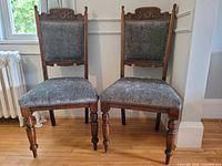 Front view of two antique dining chairs side by side showing carved wood and velvet upholstery.