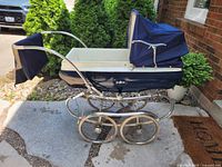 Side view of the vintage Pedigree baby carriage showing navy blue fabric exterior, folded hood, chrome frame, and large spoked wheels.