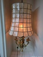 Photo of entire chandelier lit, showing shell shade and metal arms with candle holders hanging.