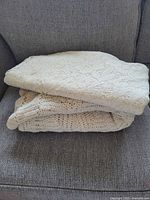 Folded view of two cream-colored vintage lace and crocheted tablecloths.