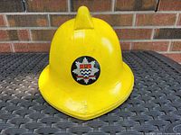 Yellow British fire helmet with London Fire Brigade emblem front center, showing helmet's shape and condition