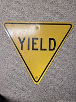 Front of the triangular yellow metal YIELD street sign showing black lettering and three mounting holes.