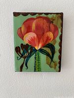 Front view of small floral painting with large red and orange flower, green leaves, scalloped pattern on edge.