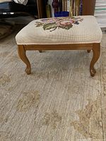Side view of wooden footstool showing carved legs and embroidered top.