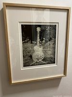 Framed black and white photograph showing the full guitar and frame hung on a wall.