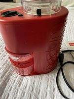 Side view of Bodum electric coffee grinder showing vibrant red body, clear grounds container, power cord.