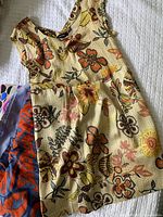 Beige floral dress with orange, brown, and purple flowers displayed on white background fabric
