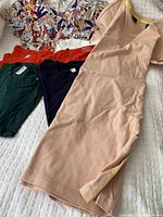 Photo showing five clothing items laid out on white textured surface: beige Club Monaco dress, colorful patterned top, dark green, navy blue, and red cotton T-shirts.