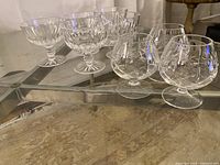 Full view showing 4 coupe glasses and 4 snifter glasses with detailed cuts, arranged on glass table.