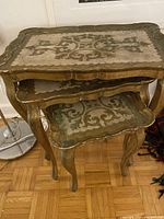 Three stacked Florentine nesting tables showing detailed floral painted tops with gold and green tones and curved cabriole legs