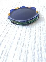 Stacked view of four flower-like shaped glass plates in blue, green, yellow, and red.