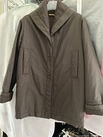 Front view of the brown nylon cocoon coat by Gigli hanging on a hanger showing full length with the collar and pockets visible.