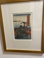 Full view of the woodblock print showing a woman in traditional kimono seated on a veranda with a lake and distant shore in background, framed in light wood.