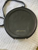 Front view of the black circular bag with ANNICK LEVESQUE embossed in gold lettering on the front.