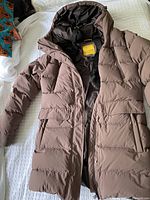 Full view of taupe hooded down coat laid out flat showing front zipper and pockets.