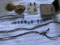 Top down view of all jewelry showing brooches, earrings on cards, and necklaces spread on fabric background.