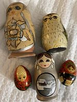 Five hand-painted wooden nesting dolls featuring owls and a silver female figure, along with two painted eggs, arranged together.