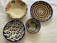 Four assorted vintage art pottery bowls viewed from top showing decorative patterns including floral, skulls, and geometrical designs.