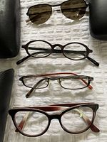 Top to bottom view of four pairs of eyewear: Valentino sunglasses, Paul Smith brown oval glasses, Matsuda rectangular glasses, Costume National cat-eye glasses