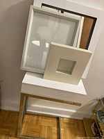 Three picture frames and Crate and Barrel mirror resting on the white side table.
