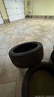 Photo of two tires stacked on tiled floor showing tread and size, in a garage.