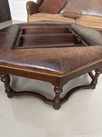 Close-up angle of octagon coffee table showing leather padded top, brass nailhead trim and carved wooden legs.