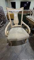 Front view of the wood dining chair showing carved backrest and beige upholstered seat cushion.