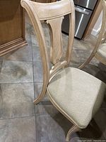 Side view of wood dining chair showing curved backrest, decorative panel, and beige fabric seat cushion.