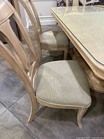 Photo showing a natural wood dining chair with an upholstered beige seat and curved backrest with slats