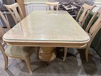 Photo showing natural wood rectangular dining table with glass top protector and six matching chairs in beige fabric.