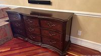 Full view of dark wood 9-drawer dresser with curved front and decorative handles placed against a wall.