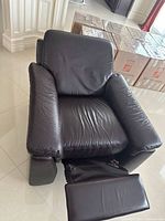 Dark brown leather reclining chair with visible creases on seat and cushioned armrests, footrest partially extended.