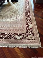 Close-up of one corner showing cream field, muted red geometric border, and cream fringe