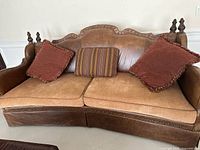 View of the sofa showing leather backrest, carved wood frame, fabric seat cushions, and three cushions on the seating surface.
