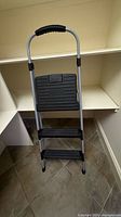 Photo of a metal step stool with two black steps and a silver frame, including a padded handle for support.