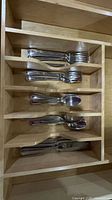 Photo of a wooden utensil drawer organizer containing six stainless steel utensils including forks, knives, and spoons.