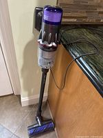Cordless stick vacuum attached to wall mount charger next to kitchen counter