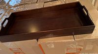 Photo of the dark brown wooden tray showing its shape, handles, and finish, placed on top of cardboard boxes.