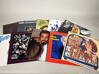 Ten vinyl albums laid out on a white surface, showing cover art and jackets. Includes ABBA Greatest Hits and others.