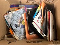 View down into a cardboard box filled with multiple 7 inch 45 RPM vinyl records with some colorful paper sleeves visible.