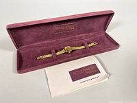 Full view of women's Bulova Accutron watch inside purple velvet-lined box alongside owner's guide booklet.