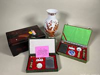 Overview of lot with porcelain vase, two rectangular green fabric covered calligraphy sets, and dark wooden jewelry box.