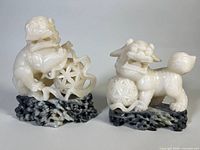 Two carved stone lion figures standing on dark carved stone bases, showing front view detailing of figures and bases.