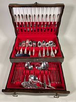 Full view of open wooden chest showing two layers of organized silverware with red felt lining.
