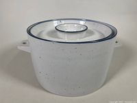 Side view of the covered casserole dish showing the white stoneware with blue rim and speckled Blue Mist pattern.