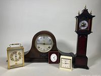 Group shot of five clocks with varied sizes and materials on white backdrop.