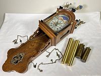 Clock laid horizontally showing wooden case, pendulum, and brass weights.